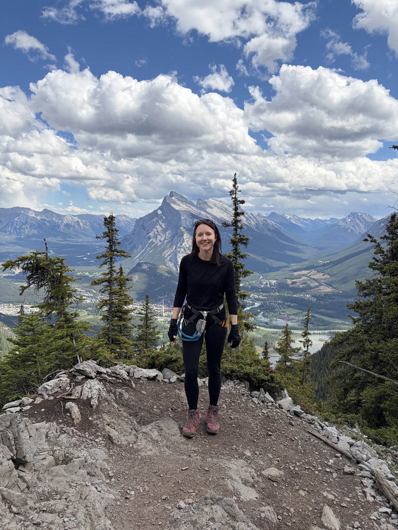 Michelle Walstra in a climbing harness above Banff, Alberta, with Mt. Rundle behind her