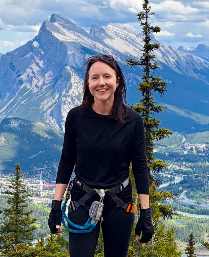 Michelle Walstra on the Mount Norquay via ferrata above Banff, Alberta - climbing harness on, Mt. Rundle behind her